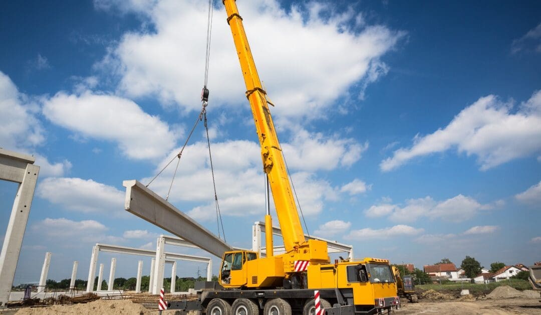 A yellow mobile crane lifts up a giant slab of concrete on a worksite with other construction materials in the background.