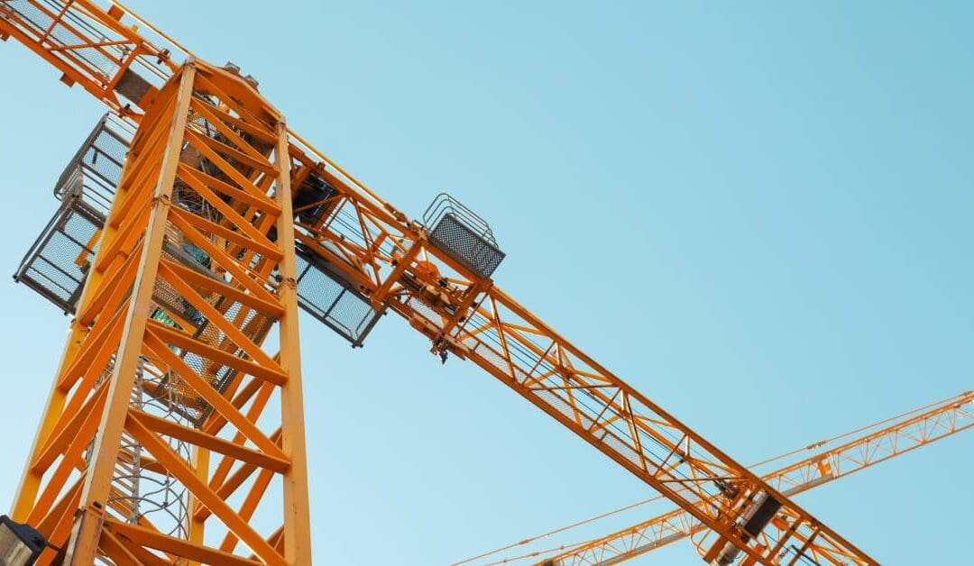 A look up at different cranes against the blue sky with no clouds. The large yellow cranes are huge, going far into the sky.