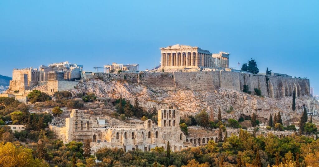 An aerial view of Athens, Greece. the Parthenon sits on a hill with other buildings and greenery below it.