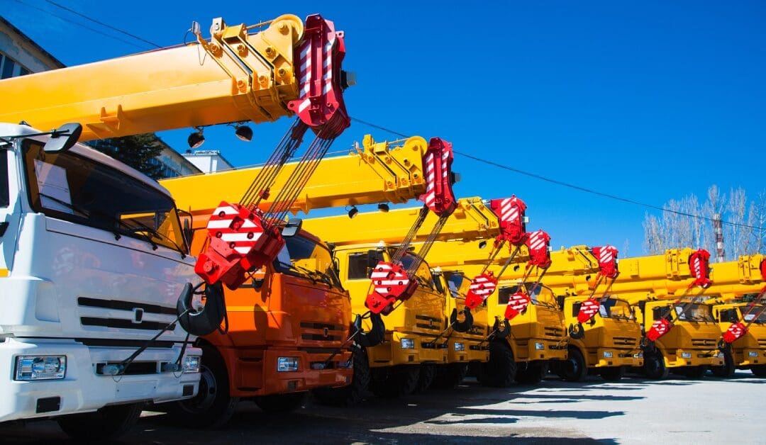 A fleet of mobile construction crane vehicles are all lined up. One is white, one is orange, and the others are all yellow.