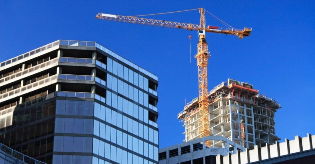 A tall crane stands next to two unfinished buildings. The sky is dark blue behind the buildings and the crane.