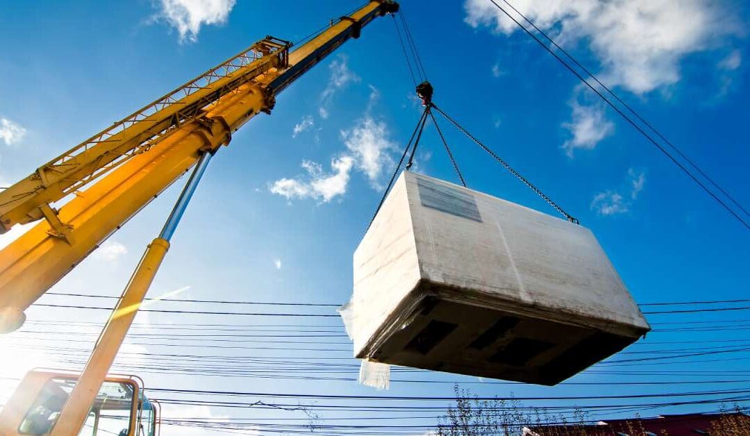 A large yellow crane is holding up a massive rectangular box against a sky with a few clouds here and there.