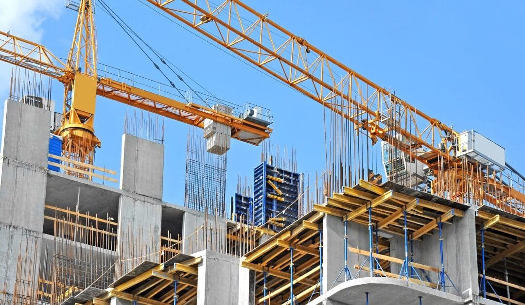 A large building is under construction with numerous cranes, scaffolding, and other equipment on the unfinished roof.