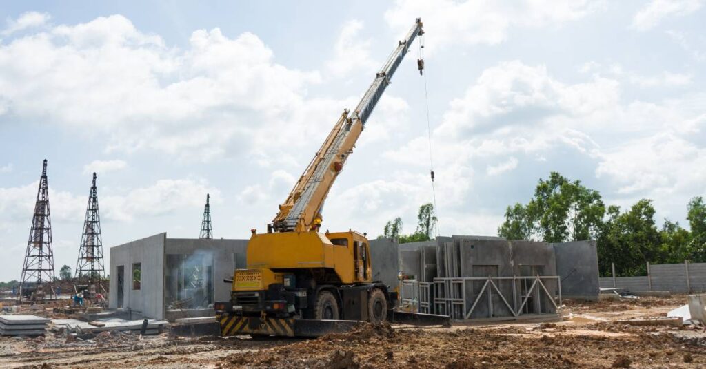 A mobile crane on a construction site with concrete poles. Around the site, the dirt has been flattened for work.