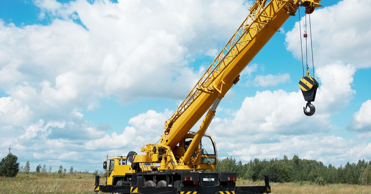 A mobile crane unit with a large hook attached to the end. The crane is sitting in a large grass field.