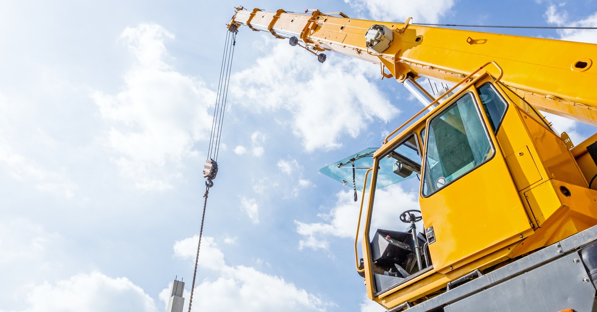 A yellow mobile crane truck with the car door left open. There is no one visible inside the crane unit.