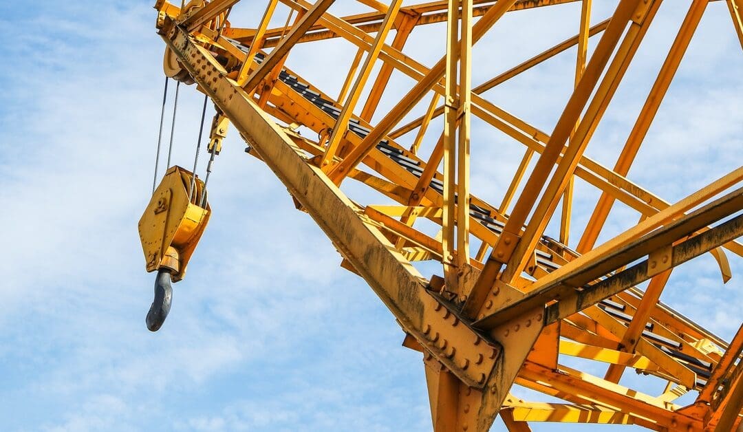 A yellow crane with a ladder heading to the top of it, where a large, sturdy hook is attached to the end.