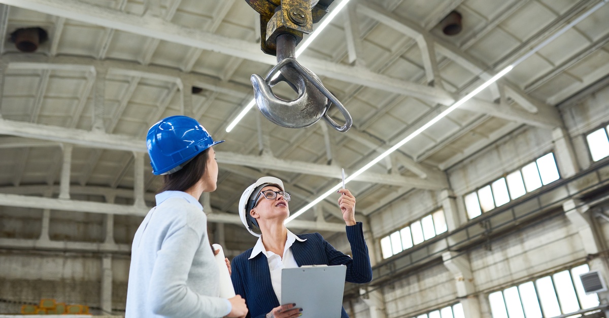A female investor and another person looking at the rigging component of a crane. Both women have hard hats on.