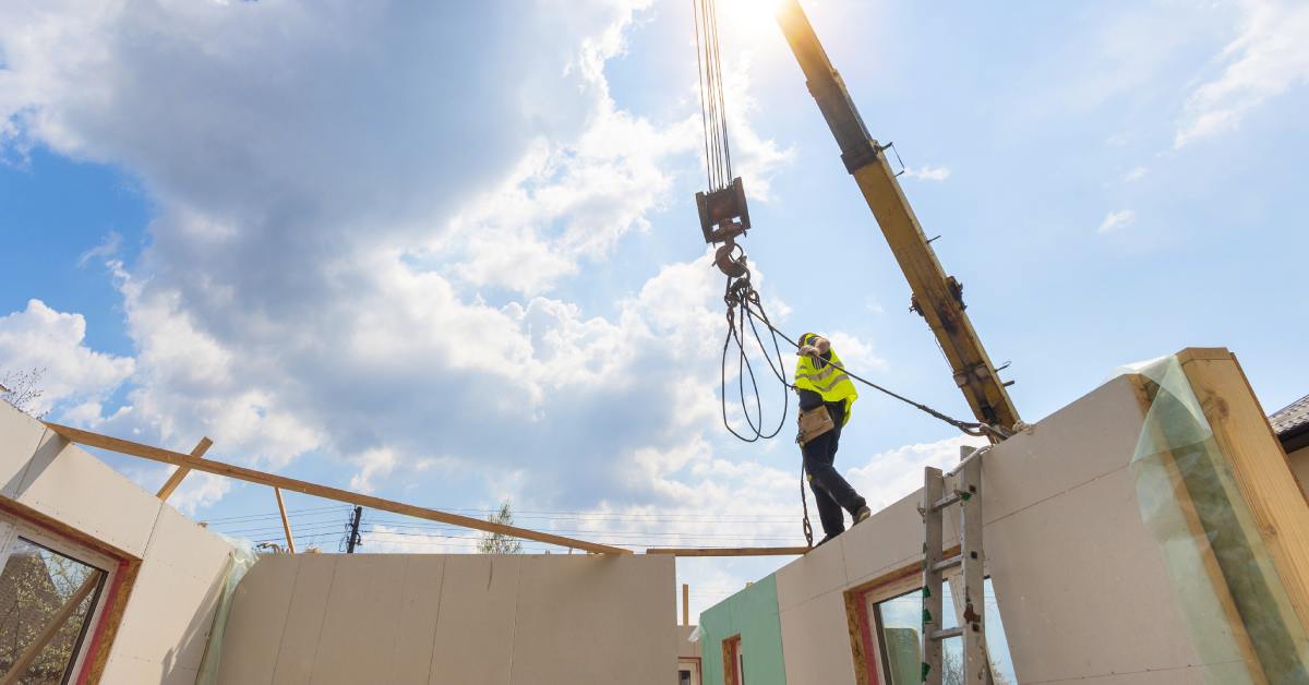 A construction crew member walking along the top of a partially constructed wall with a crane behind him.