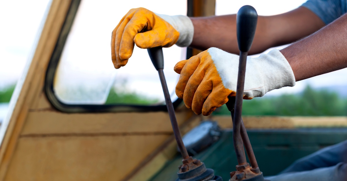 The hands of a person operating a crane. They are wearing gloves on both hands and are holding two levers.