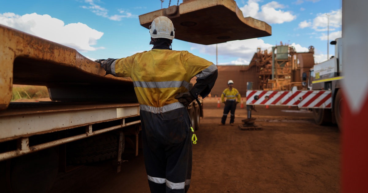 A supervisor in safety gear conducts a crane lift for a large piece of material on a construction site.