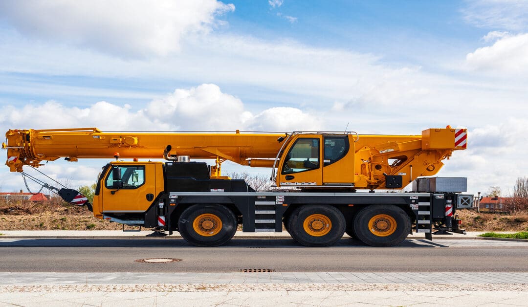 A heavy-duty mobile crane parked on the side of a road on a clear day. The crane is lowered to sit on top of the truck.