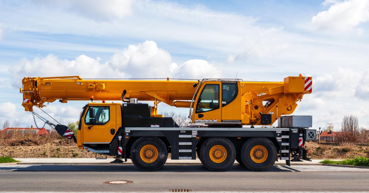 A heavy-duty mobile crane parked on the side of the road. The crane is lowered completely onto the truck.