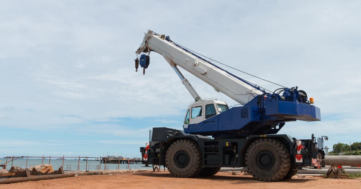 A mobile crane with the crane and rigging lowered. The machinery is waiting near a body of water to begin work.