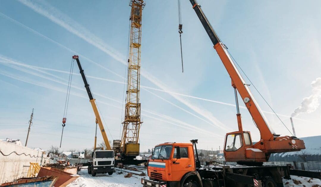 A construction site in the wintertime with snow on the ground. Several truck cranes are working on the site.
