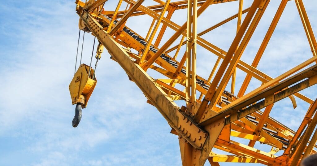 A large yellow crane with a hook attached to the end to lift items. The sky above is slightly cloudy.