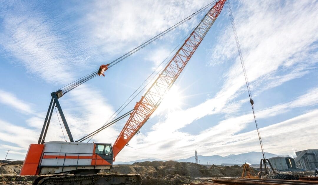 A big crawler crane on a construction site extended into the air to pick up materials lying on the ground.