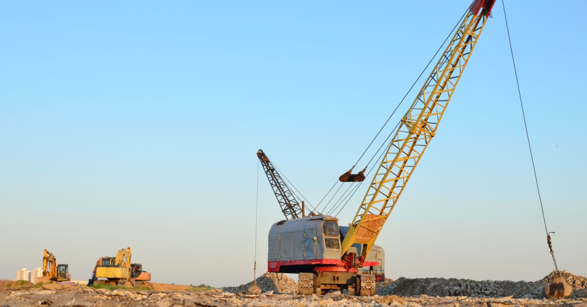 A large crawler crane with a wrecking ball on a worksite with uneven and rough ground around the equipment.